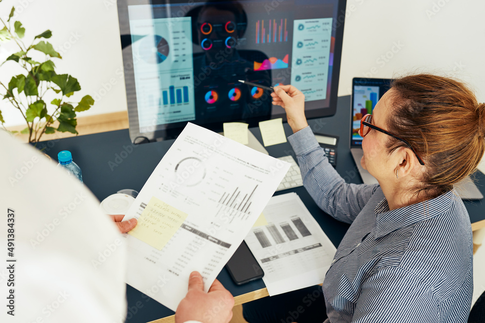 Woman entrepreneur discussing financial data with her colleague sitting at desk in office. Happy positive businesswoman working with charts and tables on computer. Two people working together Woman entrepreneur discussing financial data with her colleague sitting at desk in office. Happy positive businesswoman working with charts and tables on computer. Two people working together