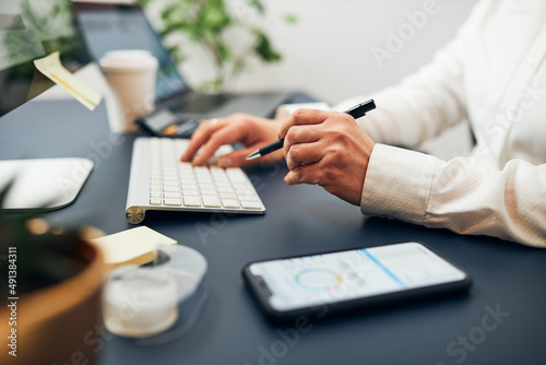 Businesswoman typing on keyboard. Entrepreneur working with data on charts, graphs and diagrams on computer and smartphone. Woman sitting at desk in office