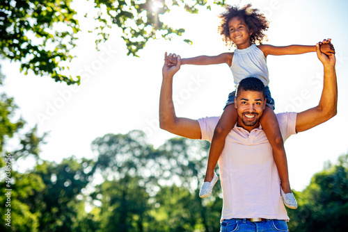 Portrait of happy black father carrying daughter on back outdoors. Family happiness love concept.