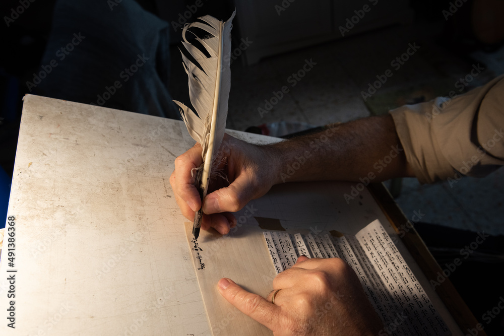 Closeup view of the hands of a Jewish scribe holding a feather quill