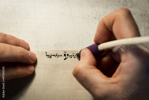 Closeup view of the hands of a Jewish scribe writing the words of the Shema Yisrael prayer on parchment that will be encased in a mezuzah and placed on the door of a Jewish home. photo