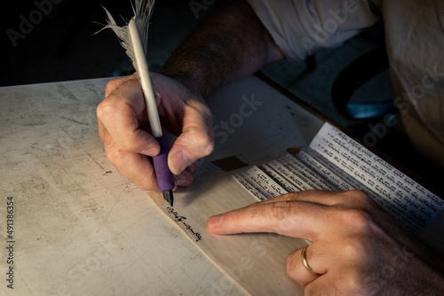 Foto Closeup view of the hands of a Jewish scribe holding a feather quill and writing the words of the Shema Yisrael prayer on parchment for a mezuzah that will be placed on the door of a Jewish home