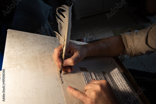 Canvas Print Closeup view of the hands of a Jewish scribe holding a feather quill and writing the words of the Shema Yisrael prayer on parchment for a mezuzah that will be placed on the door of a Jewish home