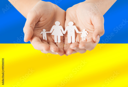 national, patriotic and charity concept - close up of hands holding family icon over colors of flag of ukraine on background