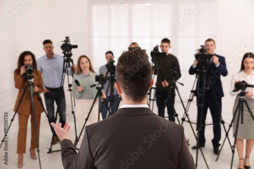 Business man talking to group of journalists indoors, back view