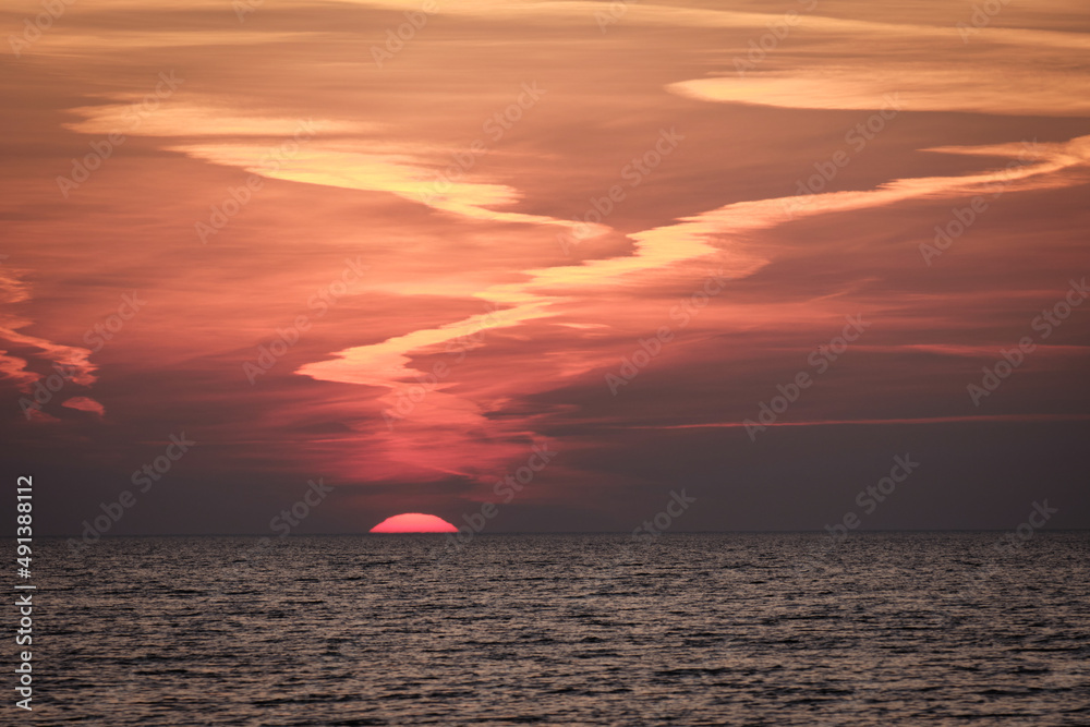 sun setting in the sea with cloud trails sun setting in the sea with cloud trails