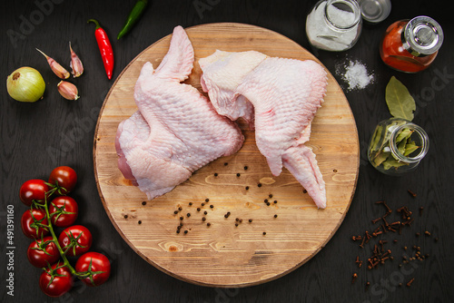 Poultry meat. Turkey wings lie on a wooden board. Chicken wing with peppers and tomatoes on a black background.