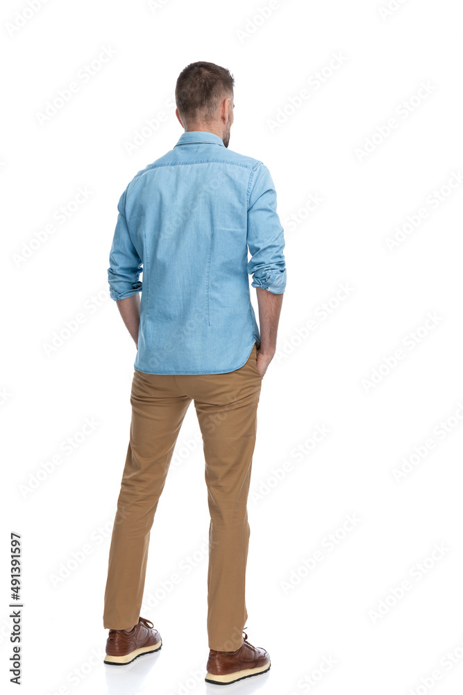 behind view of casual young guy with hands in pockets looking away behind view of casual young guy with hands in pockets looking away