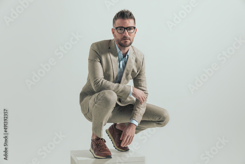 handsome unshaved man in his 40s with elbow on knee crouching photo
