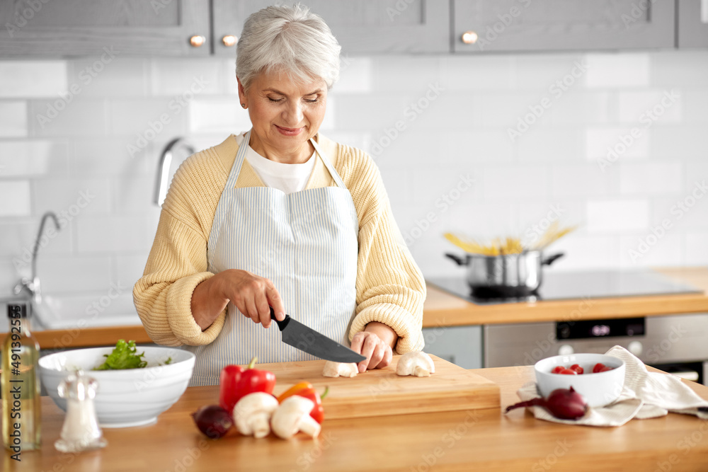 healthy eating, food cooking and culinary concept - happy smiling senior woman with knife chopping champignons on kitchen at home healthy eating, food cooking and culinary concept - happy smiling senior woman with knife chopping champignons on kitchen at home