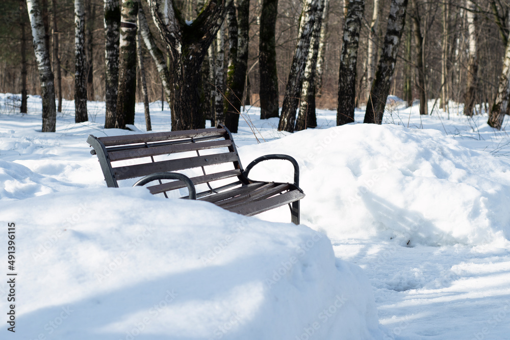 An empty bench in a winter park among large snowdrifts.