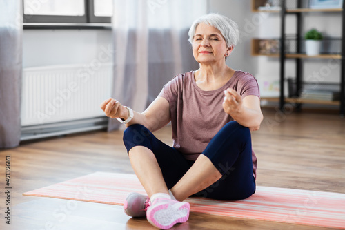 sport, fitness and healthy lifestyle concept - happy senior woman meditating on exercise mat at home