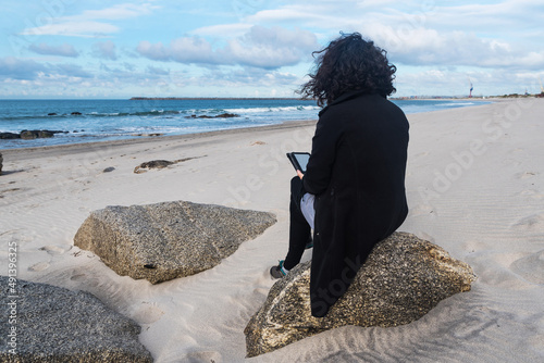 Woman with ebook reading on the beach on a cool mornin photo