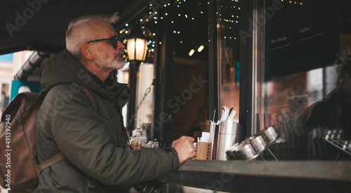 Senior man buys a drink at a street stall. Small shop customer.