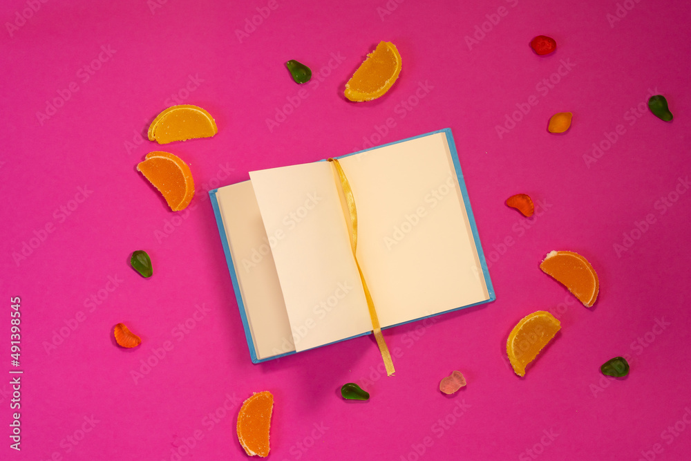 Blue blank notebook with bright jelly candies for your inscription on a pink summer background. Blue blank notebook with bright jelly candies for your inscription on a pink summer background.