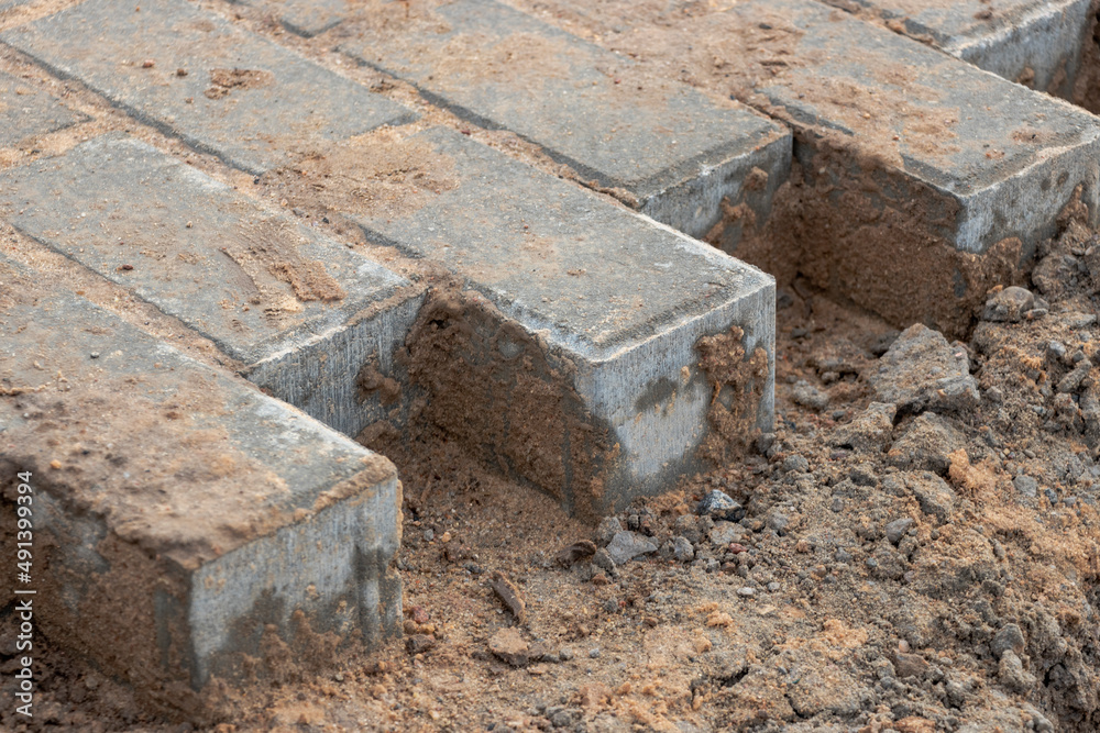 Pavement repair and laying of paving slabs on the walkway, stacked tile cubes on the background. Laying paving slabs in the pedestrian zone of the city, sand filling. Road tiles and curbs. Pavement repair and laying of paving slabs on the walkway, stacked tile cubes on the background. Laying paving slabs in the pedestrian zone of the city, sand filling. Road tiles and curbs.