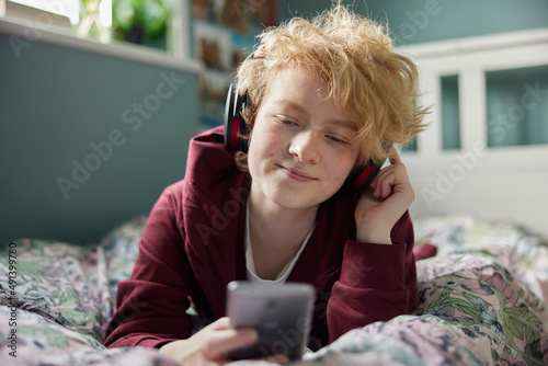 Teenage Girl Wearing Wireless Headphones Listening To Music Steaming From Mobile Phone At Home photo