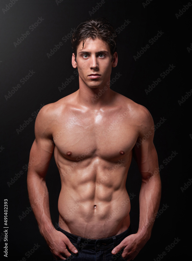 Herculean hunk. Studio shot of a handsome bare-chested young athlete standing against a black background. Herculean hunk. Studio shot of a handsome bare-chested young athlete standing against a black background.