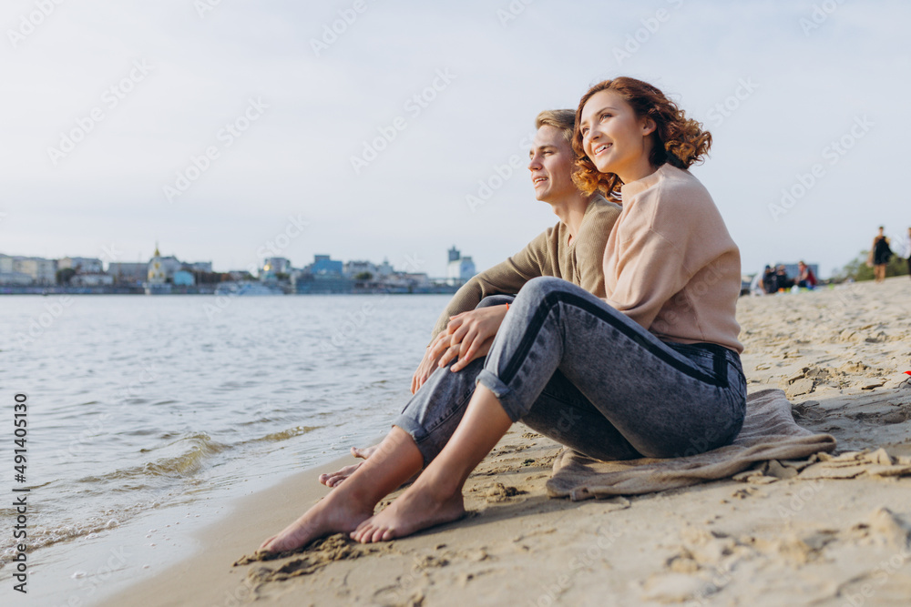 A loving couple has fun - they laugh, hug each other and enjoy a warm summer evening. Romantic couple sitting by the sea. Portrait of a guy hugging his girlfriend