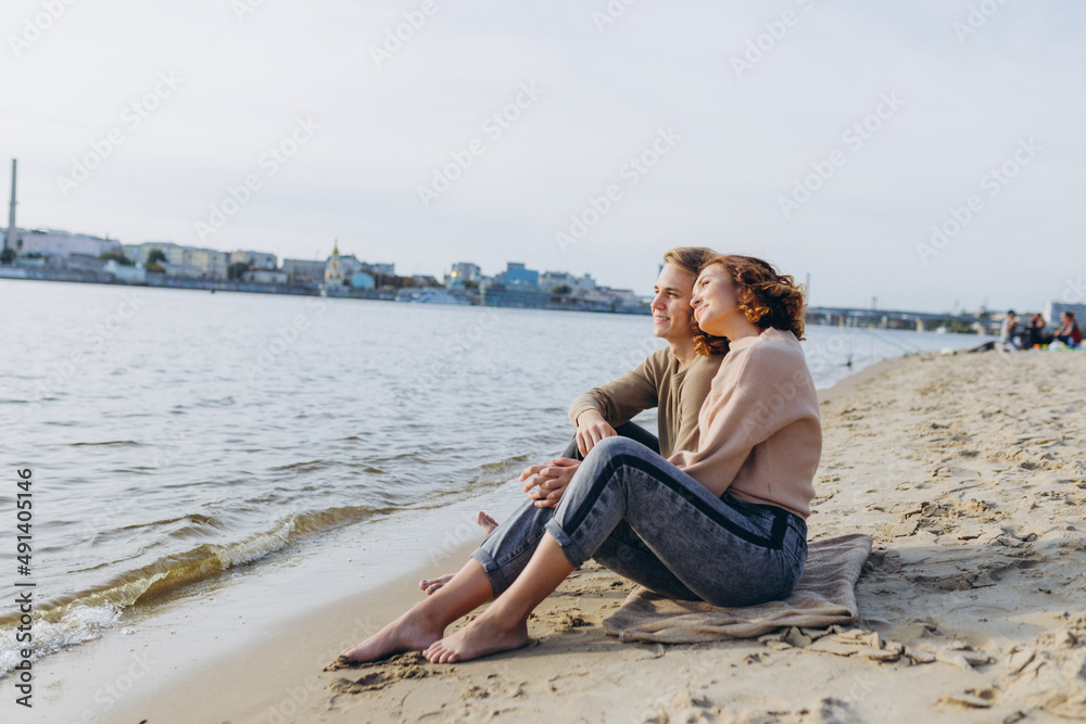 A loving couple has fun - they laugh, hug each other and enjoy a warm summer evening. Romantic couple sitting by the sea. The young guy tells interesting stories of the girl and points aside hands