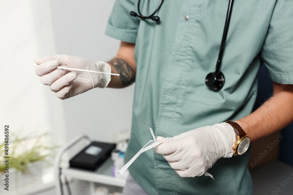 a doctor in a green coat and white rubber gloves takes a smear from a patient with a wand for analysis. testing for coronavirus infection a doctor in a green coat and white rubber gloves takes a smear from a patient with a wand for analysis. testing for coronavirus infection