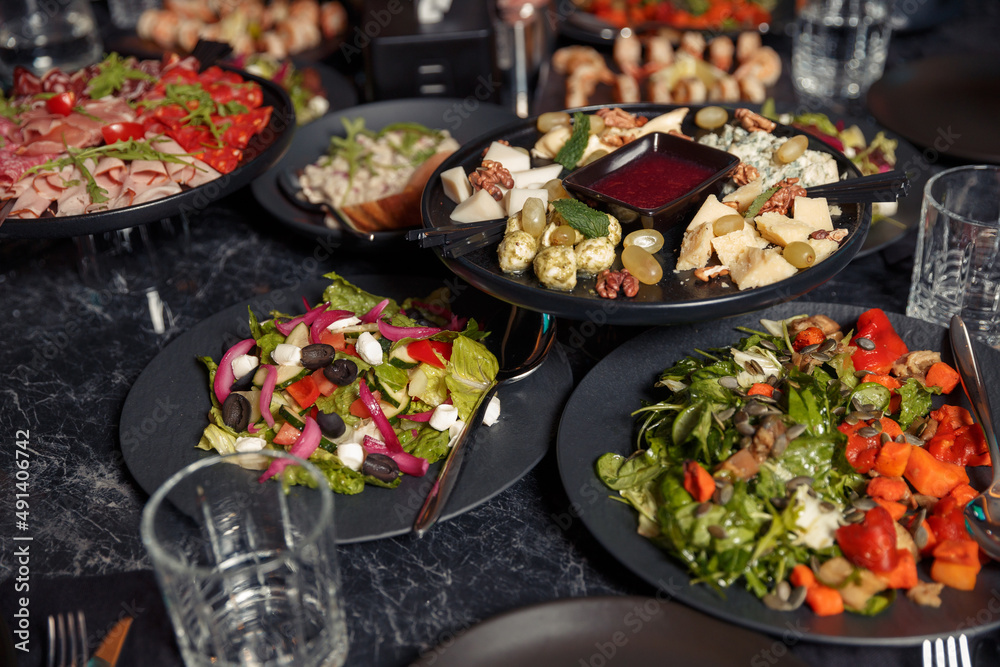 large black plates on a dark loft style table with fresh organic salads, cold cuts, prusciutto cheese. dinner at an expensive restaurant