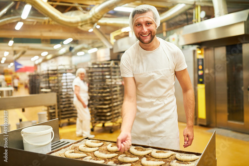 Bäcker Lehrling in der Bäckerei bestreut Croissants mit Mohn photo