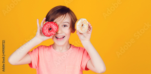 Birthday party. Tasty food for kids. Colored donuts. Fashion, people, lifestyle. Happy child played with donuts on yellow background wall.