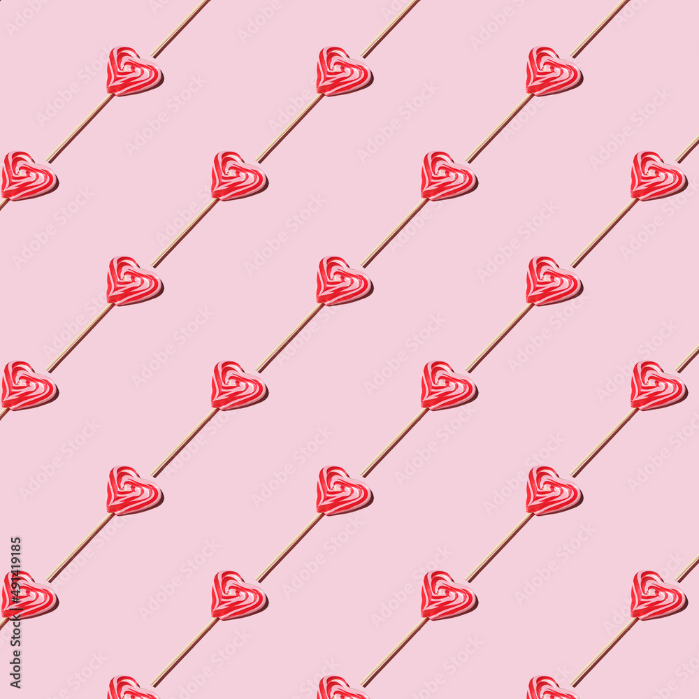 Pattern made of heart-shaped lollipops on a pink background. Repeating lollipops. Red and whie striped sweet lollipops. Flat lay style. Pattern made of heart-shaped lollipops on a pink background. Repeating lollipops. Red and whie striped sweet lollipops. Flat lay style.