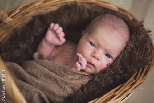 Close-up portrait of a newborn baby girl lying in a brown blanket in a basket. Happy baby