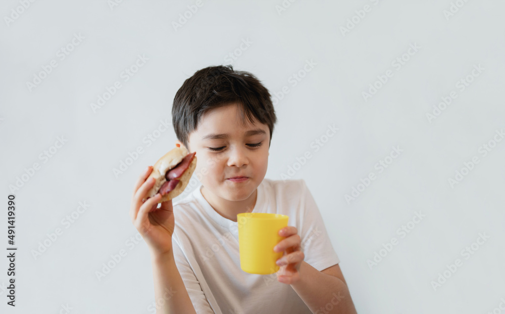 Hungry young boy eating homemade bacon sandwiches with mixed vegetables, Healthy Kid drinking juice for breakfast at home, Child bitting finger nails and looking out with thinking face Hungry young boy eating homemade bacon sandwiches with mixed vegetables, Healthy Kid drinking juice for breakfast at home, Child bitting finger nails and looking out with thinking face