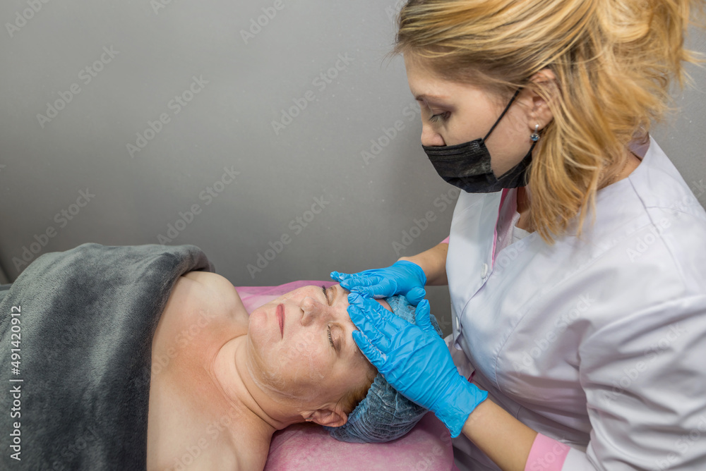 A female cosmetologist applies foam on the patient's face before a cosmetology procedure. Professional face cleaning in a beauty salon. A female cosmetologist applies foam on the patient's face before a cosmetology procedure. Professional face cleaning in a beauty salon.