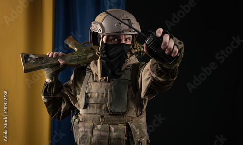 a male soldier in a military uniform and helmet with a weapon on the background of the national flag of Ukraine