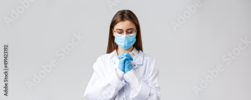 Covid-19, preventing virus, health, healthcare workers and quarantine concept. Hopeful doctor in scrubs and medical mask, personal protective equipment, praying with hands clasped together, hope photo