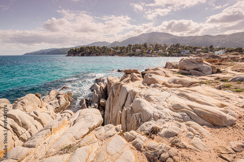 View of the picturesque scene of sea waves crashing on the rocks of a scenic island near resort town in Halkidiki region