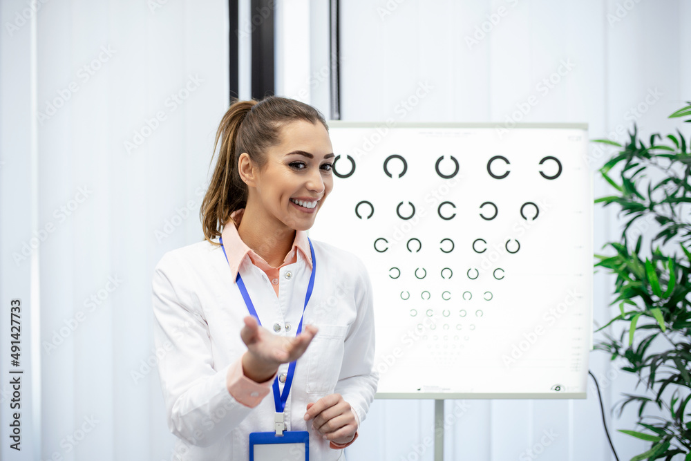 Professional female optician pointing at eye chart, timely diagnosis of vision. Portrait of optician asking patient for an eye exam test with an eye chart monitor at his clinic Professional female optician pointing at eye chart, timely diagnosis of vision. Portrait of optician asking patient for an eye exam test with an eye chart monitor at his clinic