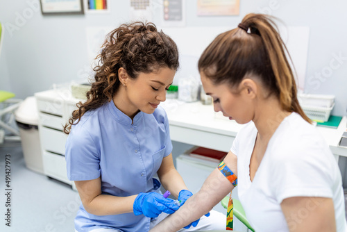 Preparation for blood test with pretty young woman by female doctor medical uniform on the table in white bright room. Nurse pierces the patient's arm vein with needle blank tube.