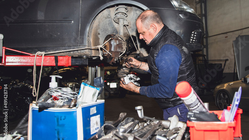 mechanic disassembling a shaft driver of raised car in crane with tools in foreground