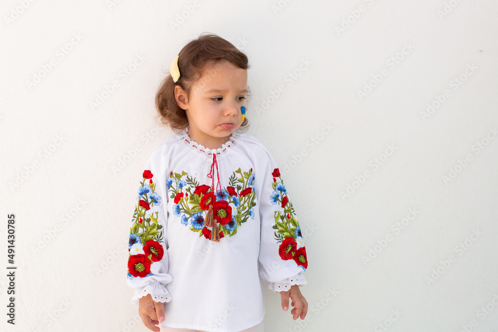 Little Ukrainian girl in an embroidered shirt on a white background. A little girl in national Ukrainian clothes - vyshyvanka. Little Ukrainian girl with a patriotic flag. Little Ukrainian girl in an embroidered shirt on a white background. A little girl in national Ukrainian clothes - vyshyvanka. Little Ukrainian girl with a patriotic flag.