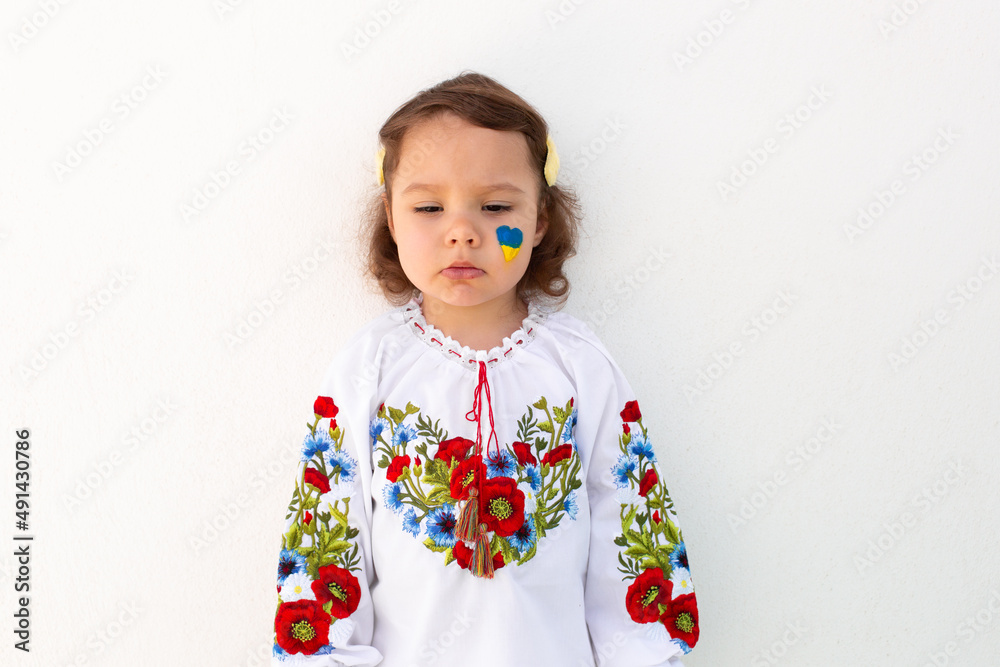 Little Ukrainian girl in an embroidered shirt on a white background. A little girl in national Ukrainian clothes - vyshyvanka. Little Ukrainian girl with a patriotic flag. Little Ukrainian girl in an embroidered shirt on a white background. A little girl in national Ukrainian clothes - vyshyvanka. Little Ukrainian girl with a patriotic flag.