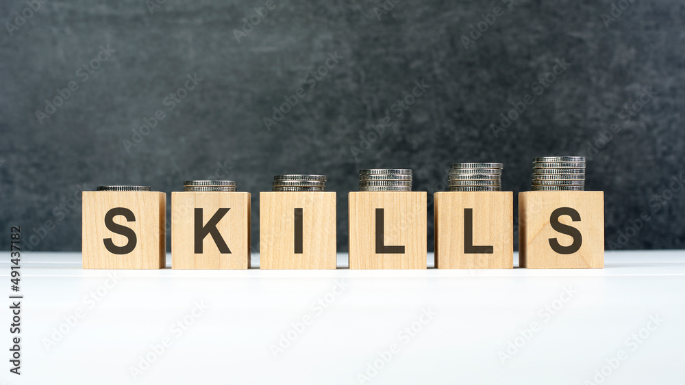 Naklejka premium SKILLS word, text written on wooden cubes on a black background with coins on cubes