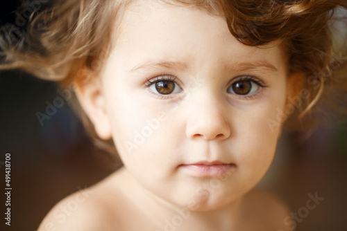 A small child looks into the camera and smiles sweetly. Toddler boy or girl portrait close-up.