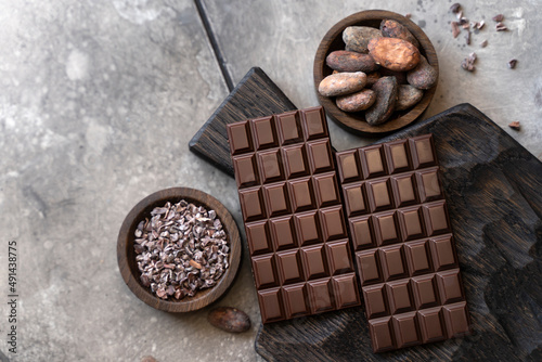 Stack of chocolate bars with cocoa beans. Flat lay composition with delicious chocolate on black background. Space for text
