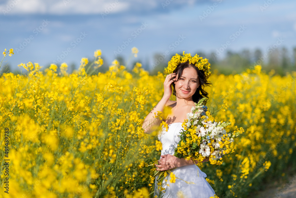 Portrait of a beautiful woman with a wreath of yellow flowers on her head. A girl with a bouquet in a rapeseed field Portrait of a beautiful woman with a wreath of yellow flowers on her head. A girl with a bouquet in a rapeseed field