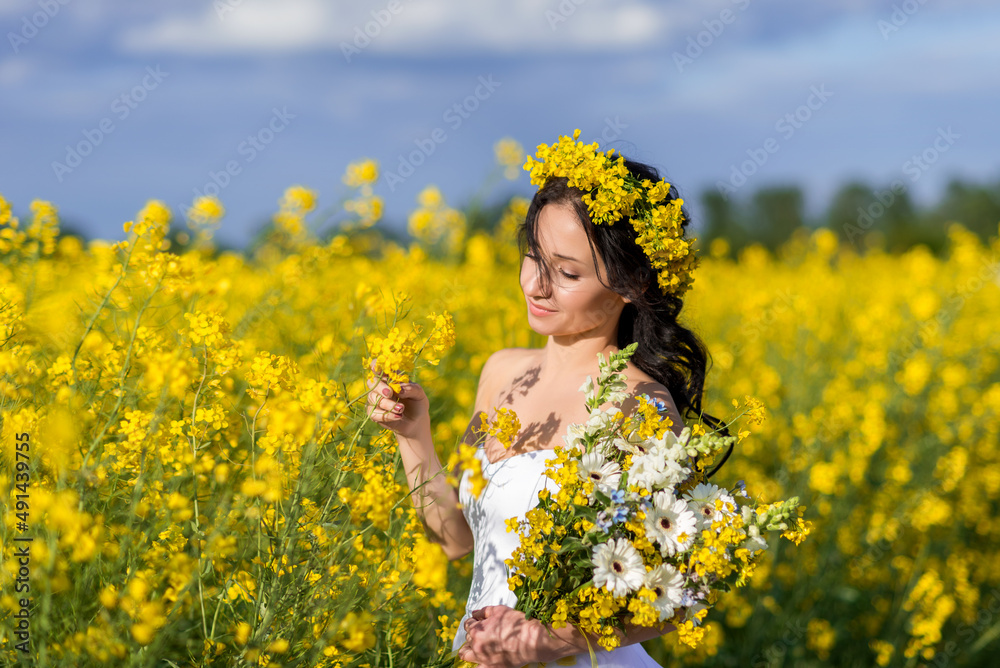 Portrait of a beautiful woman with a wreath of yellow flowers on her head. A girl with a bouquet in a rapeseed field collects flowers Portrait of a beautiful woman with a wreath of yellow flowers on her head. A girl with a bouquet in a rapeseed field collects flowers