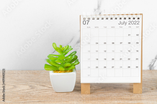 July 2022 desk calendar with plant on wooden table.