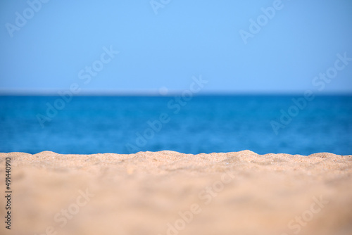 Close up of clean yellow sand surface covering seaside beach with blue sea water on background. Travel and vacations concept
