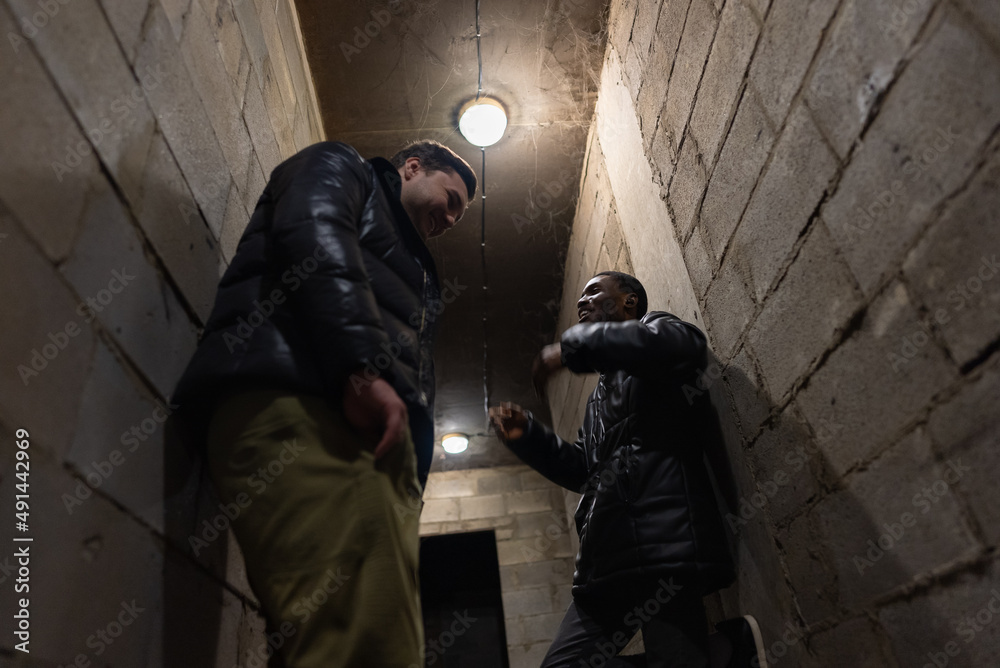 Caucasian guy and black guy are hiding in a bomb-shelter and trying to have fun during russian invasion