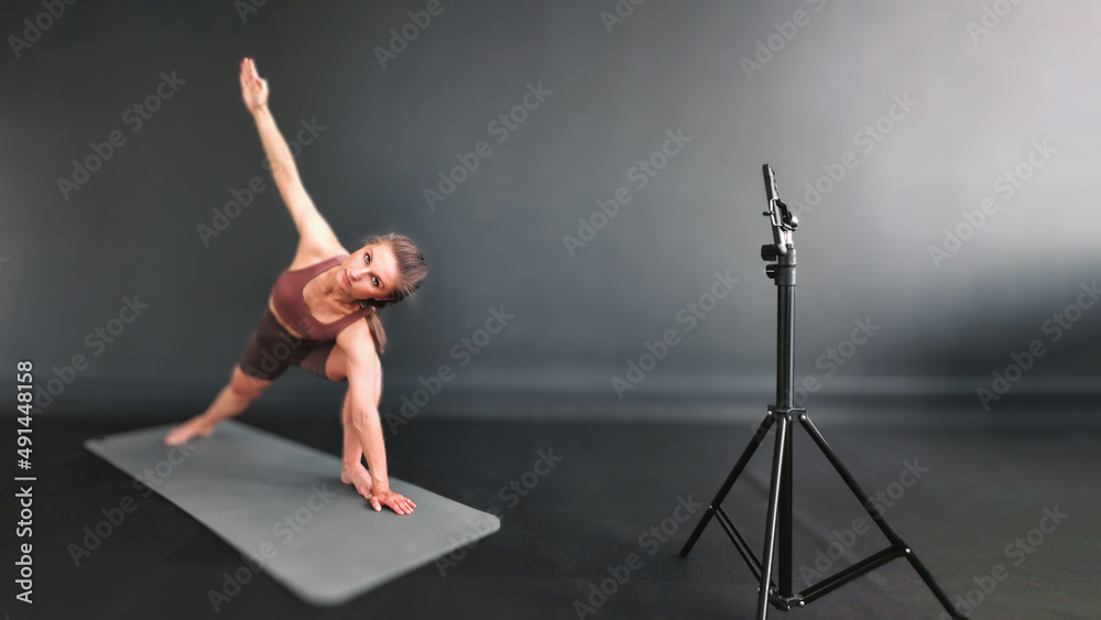 Fitness girl shows exercises master class via smartphone camera online. Fitness training remotely. The trainer records video on a smartphone. Fitness live. Online fitness classes.