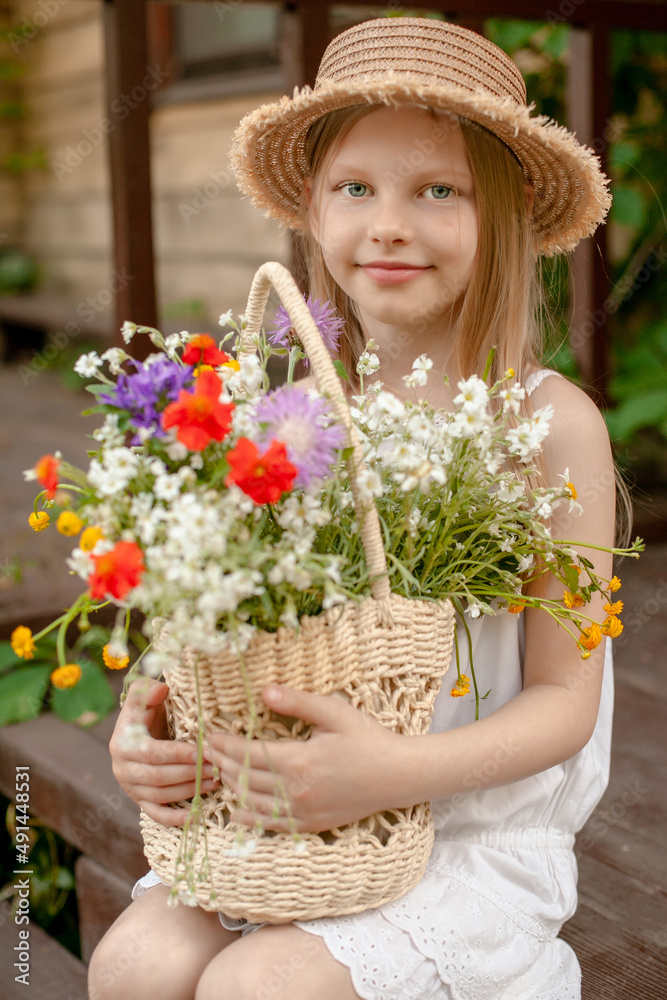 Smilingpreteen girl with basket of wildflowers sitting on threshold of rural house
